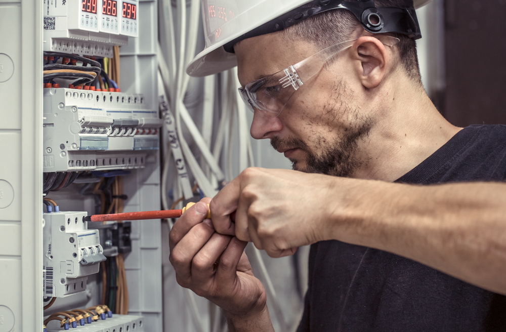 a male electrician works in a switchboard with an electrical con